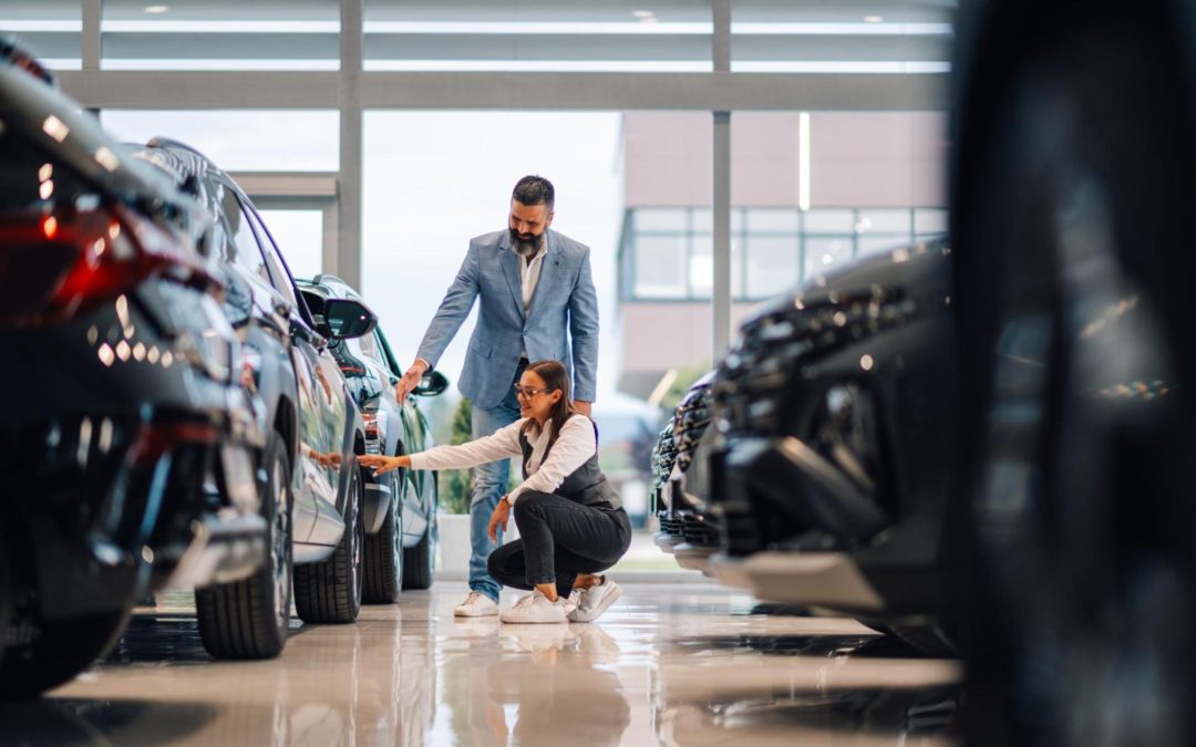 Customer in clean showroom touching new vehicle while talking to dealer