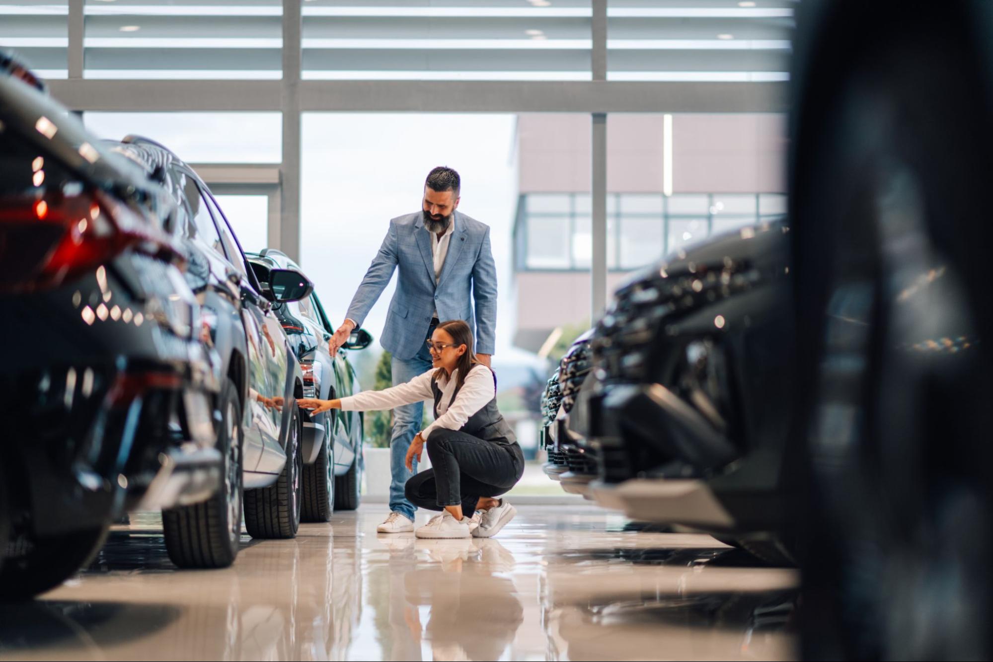 Customer in clean showroom touching new vehicle while talking to dealer