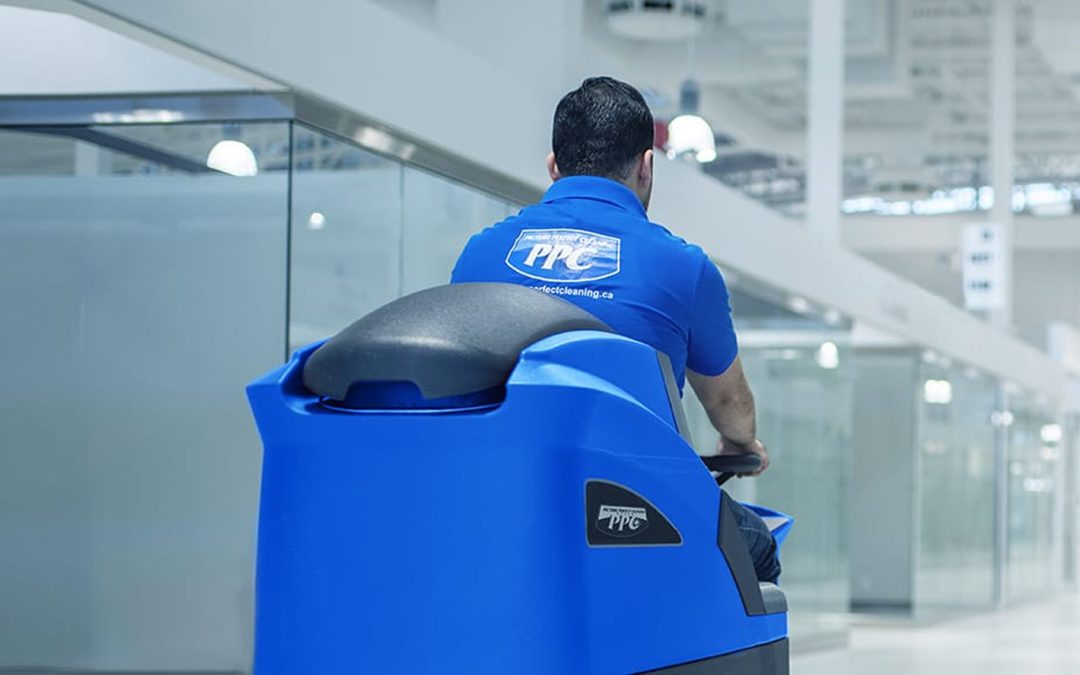 Picture Perfect Cleaning staff using a blue ride-on floor scrubber to clean a large retail or mall corridor.