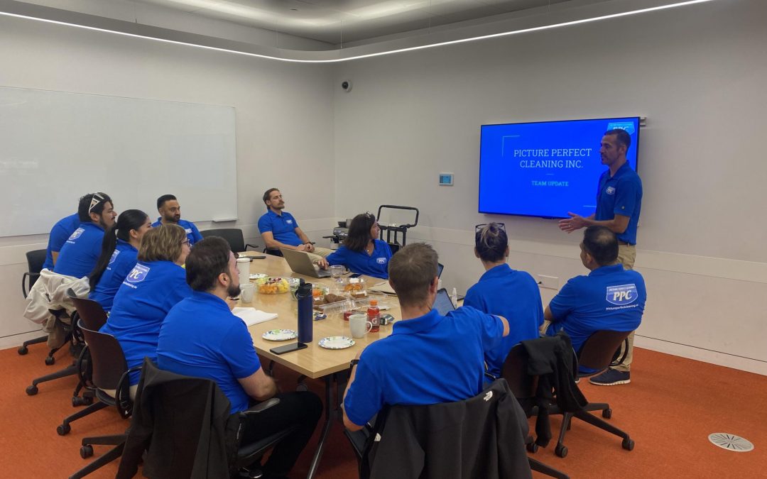 Picture Perfect Cleaning team gathered in a meeting room, discussing full-time employee health benefits with a presentation on screen.
