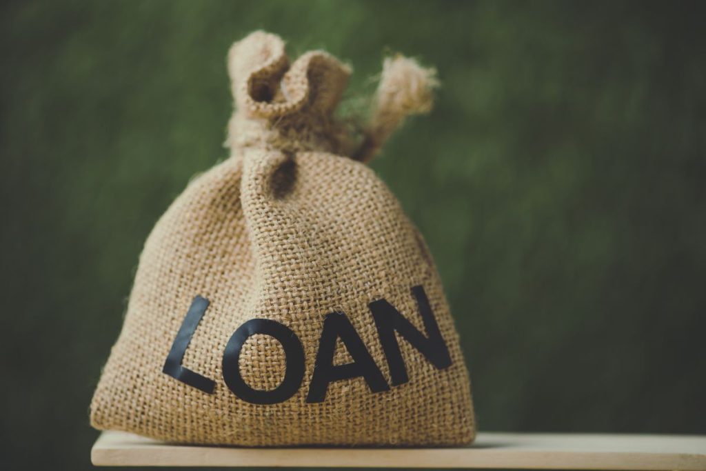 A small burlap sack with the word "LOAN" in black, sitting on a small wooden table.